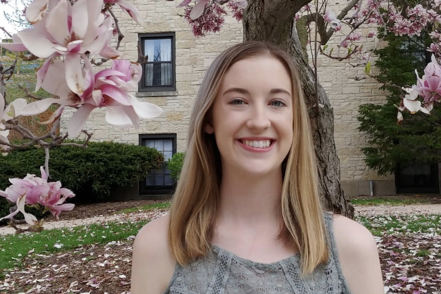 kelly quirk standing on campus beneath a flowering tree